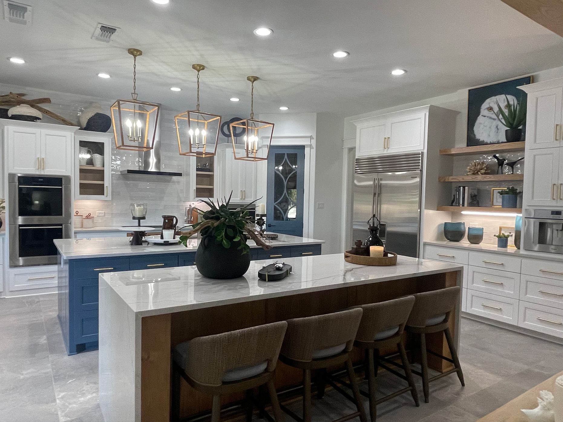 Bright modern white kitchen with blue island, pendant lights, and chairs around a central counter