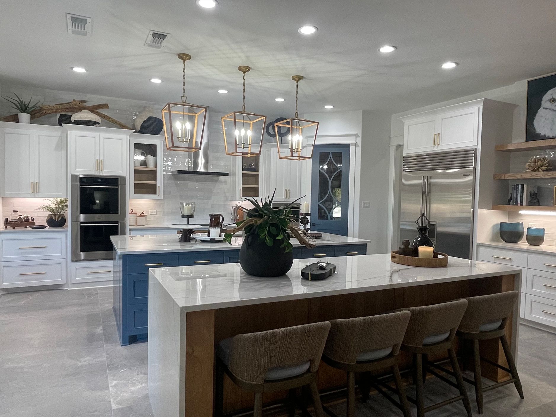 Bright modern kitchen with white cabinets, blue island, large dining table, and pendant lights