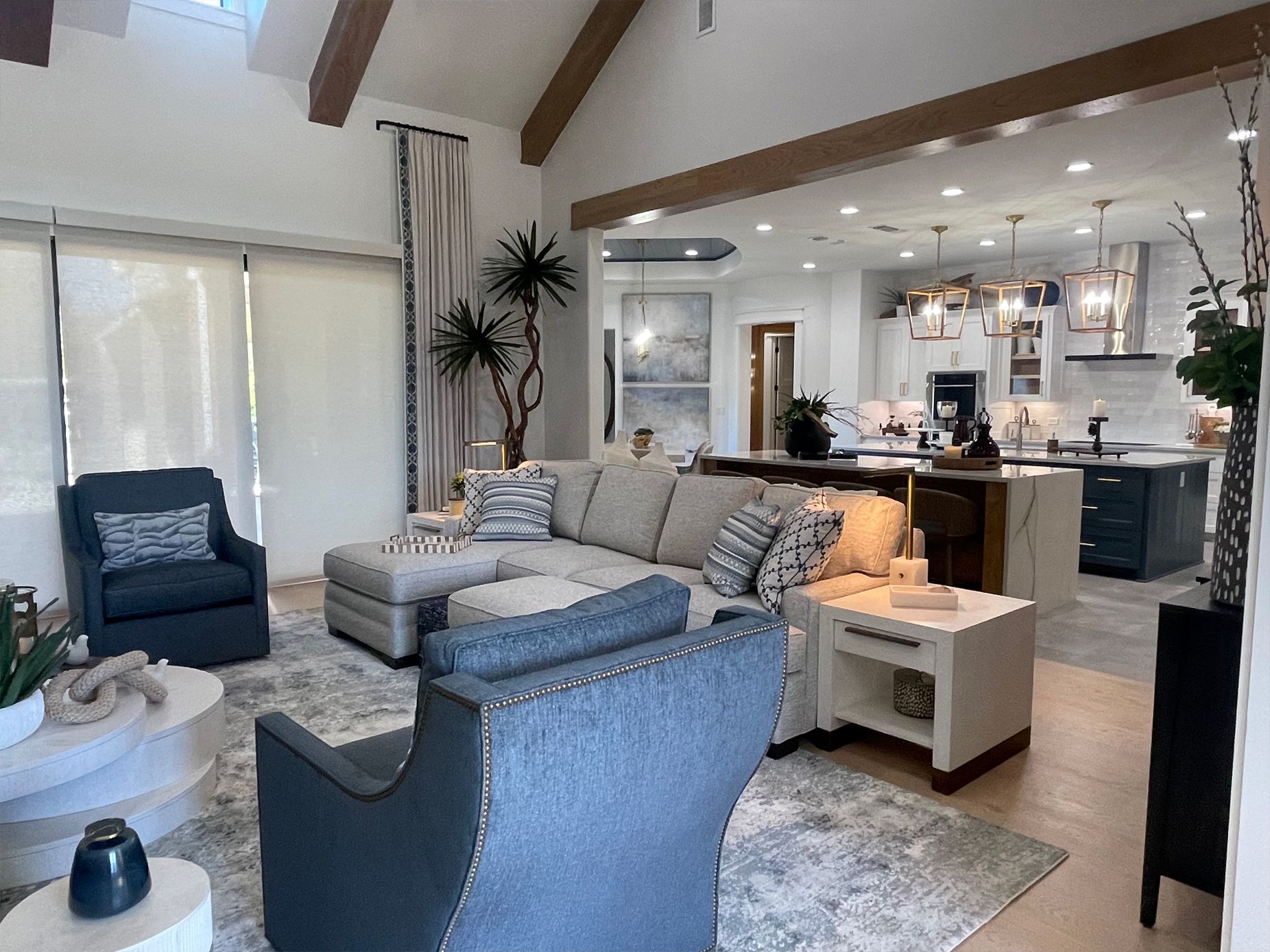 Modern open-concept living room with blue chairs, gray sofa, and kitchen in the background