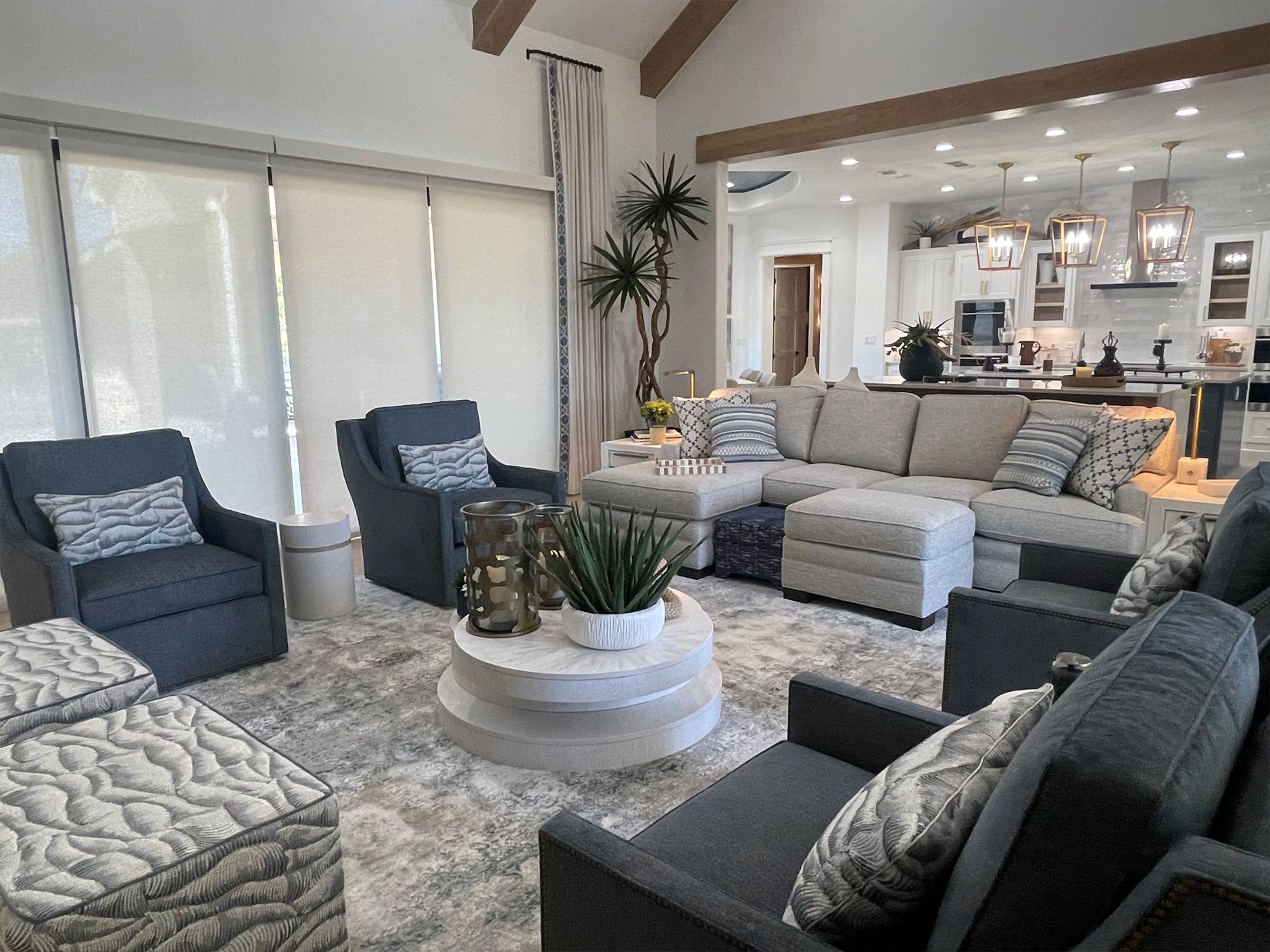 Modern living room with gray seating, patterned rug, coffee table, and open view to a kitchen