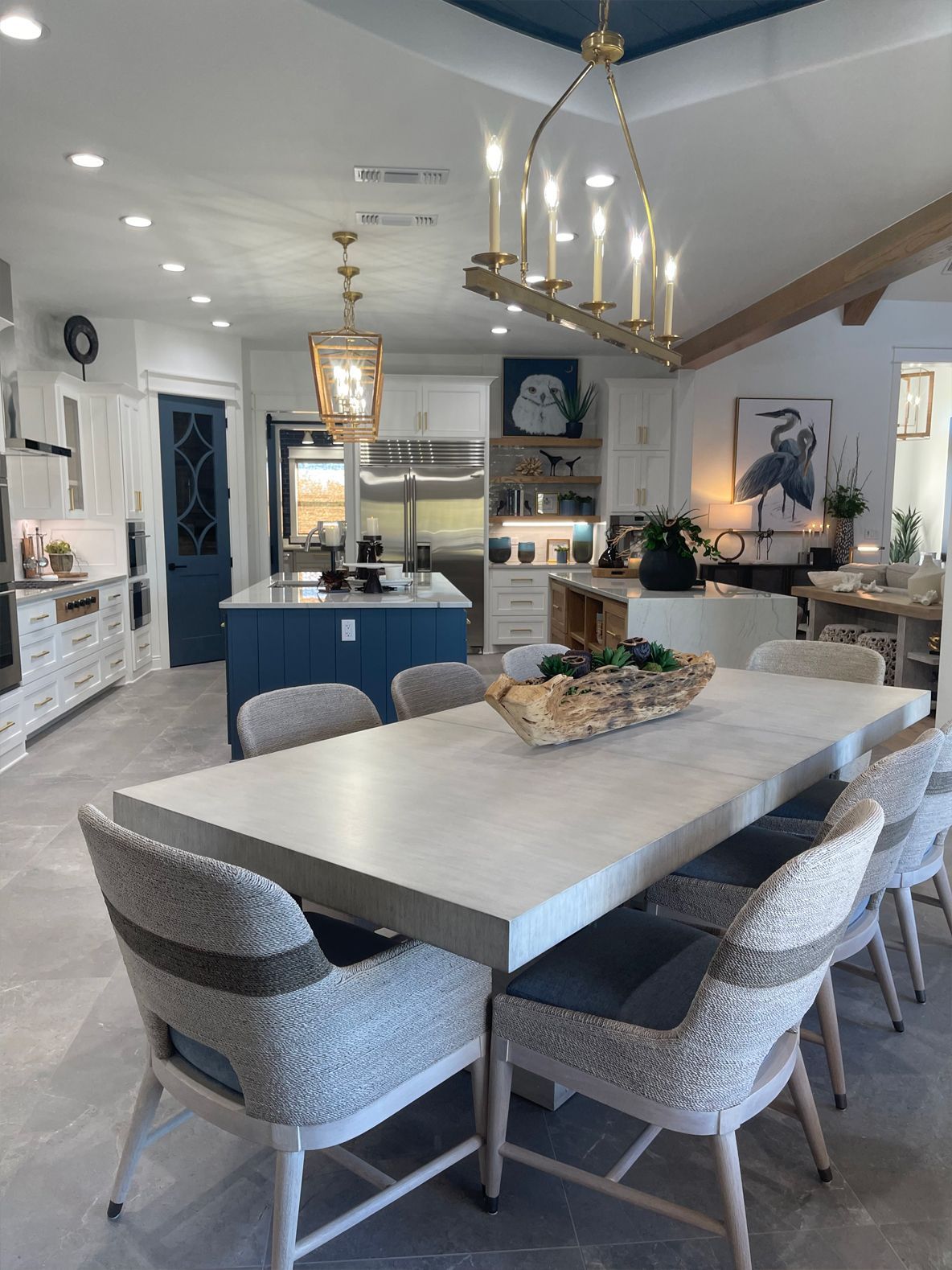 Modern kitchen and dining area with a long table, gray chairs, blue island, and pendant lighting