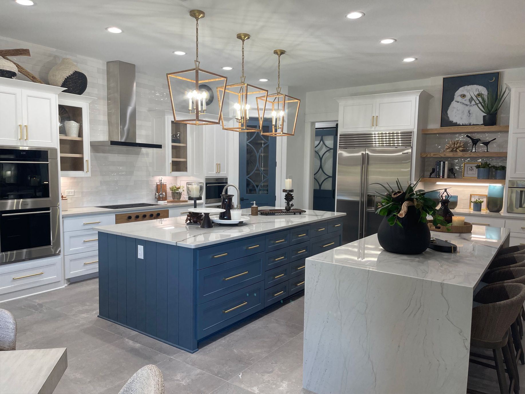 Modern kitchen with blue island, marble counters, stainless appliances, and gold pendant lights