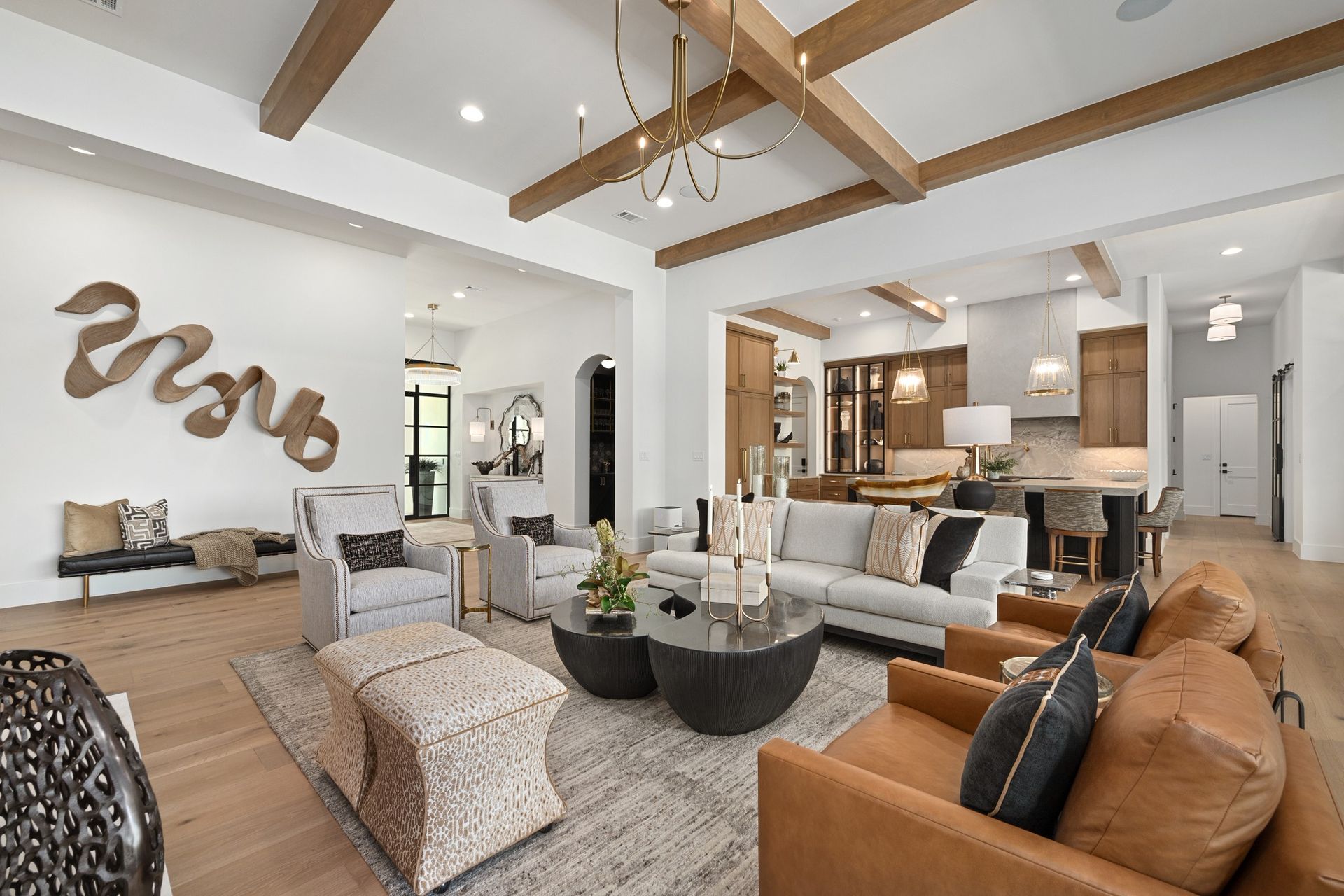 Bright modern living room with vaulted wood-beam ceiling, tan sofa, and open kitchen in the background