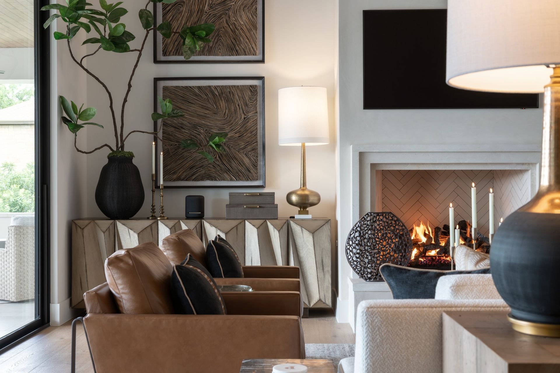 Modern living room with tan chairs, wall art, a lit fireplace, and a floor lamp