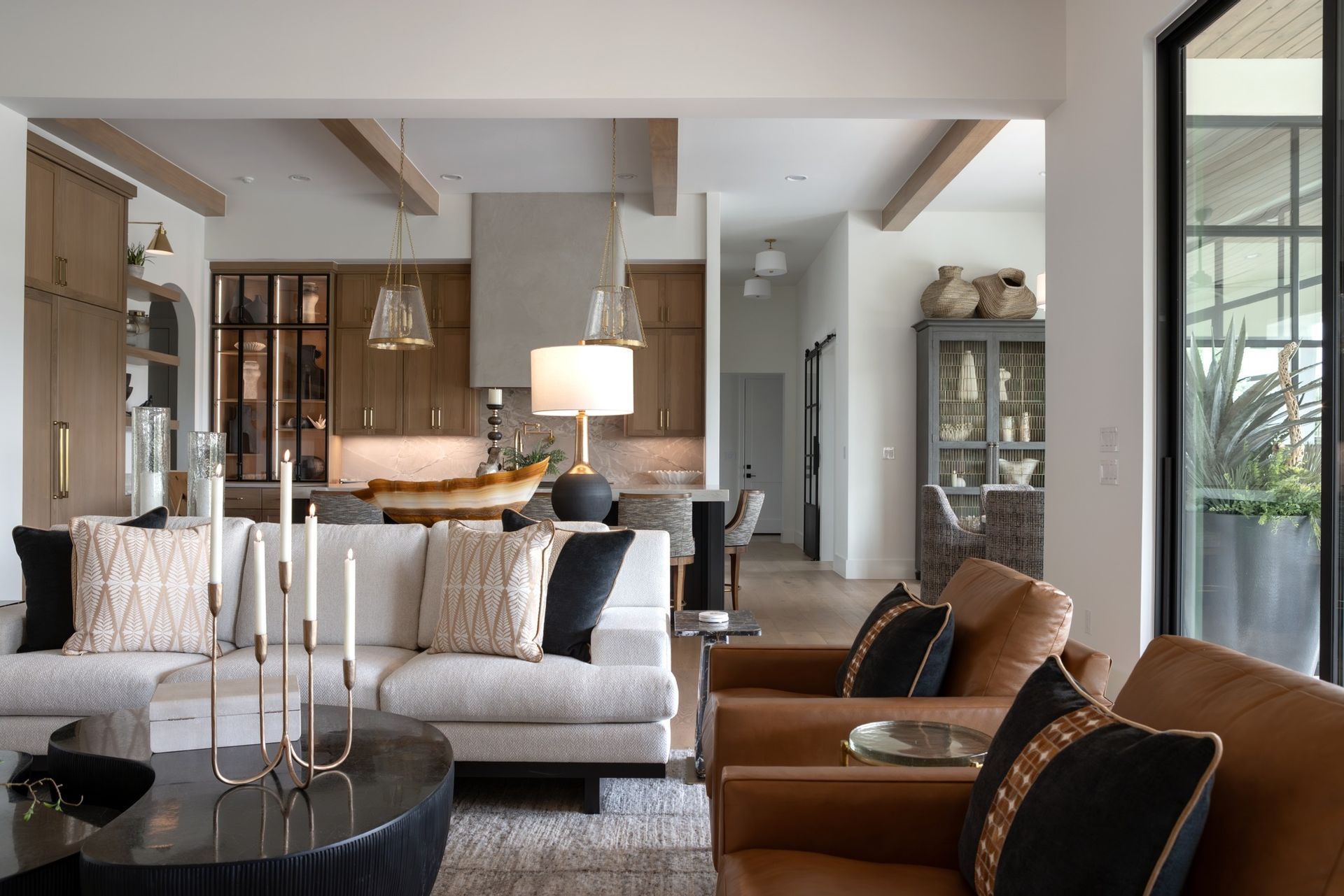 Modern living room with beige sofa, leather chairs, lamp, and open kitchen in the background