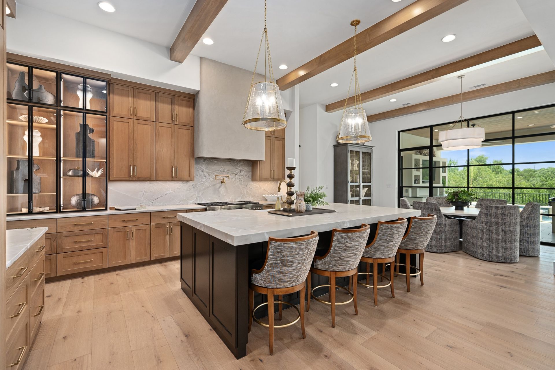 Bright modern kitchen with a large island, wood cabinets, and pendant lights overlooking a scenic window.