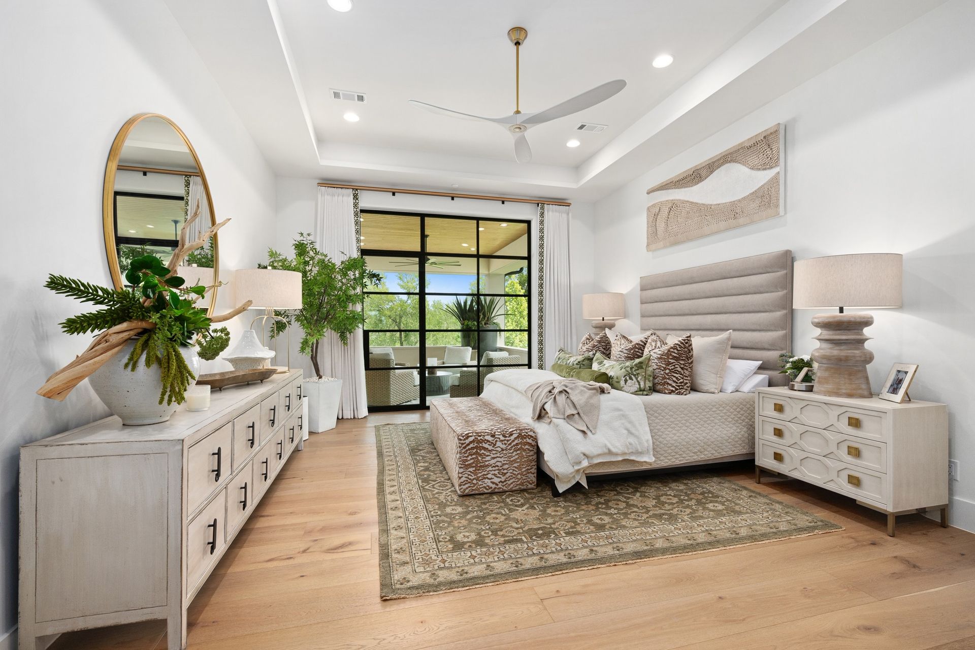 Bright modern bedroom with a large bed, white furniture, plants, and sliding doors to a balcony.