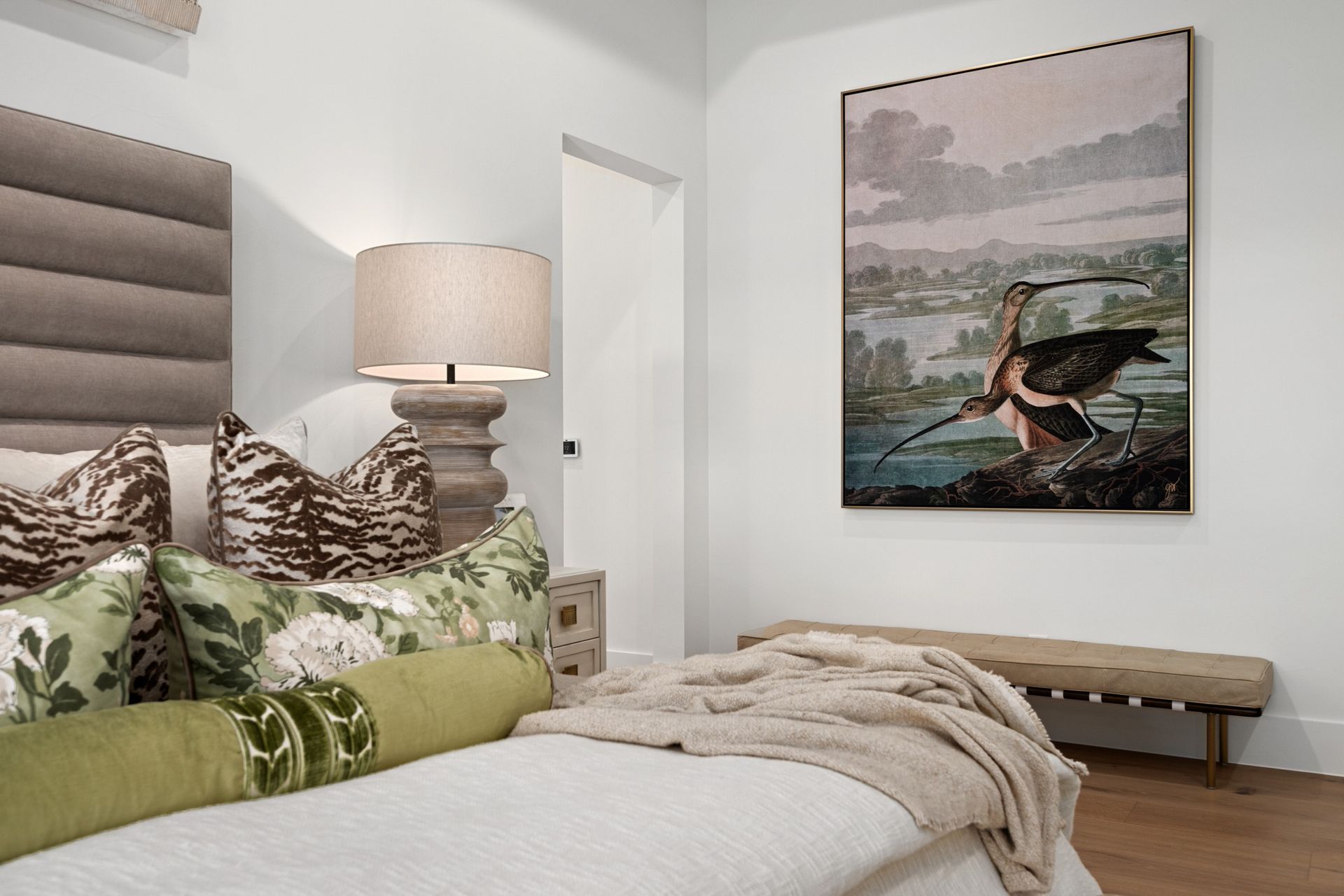 Cozy bedroom with a made bed, lamp, bench, and landscape wall art
