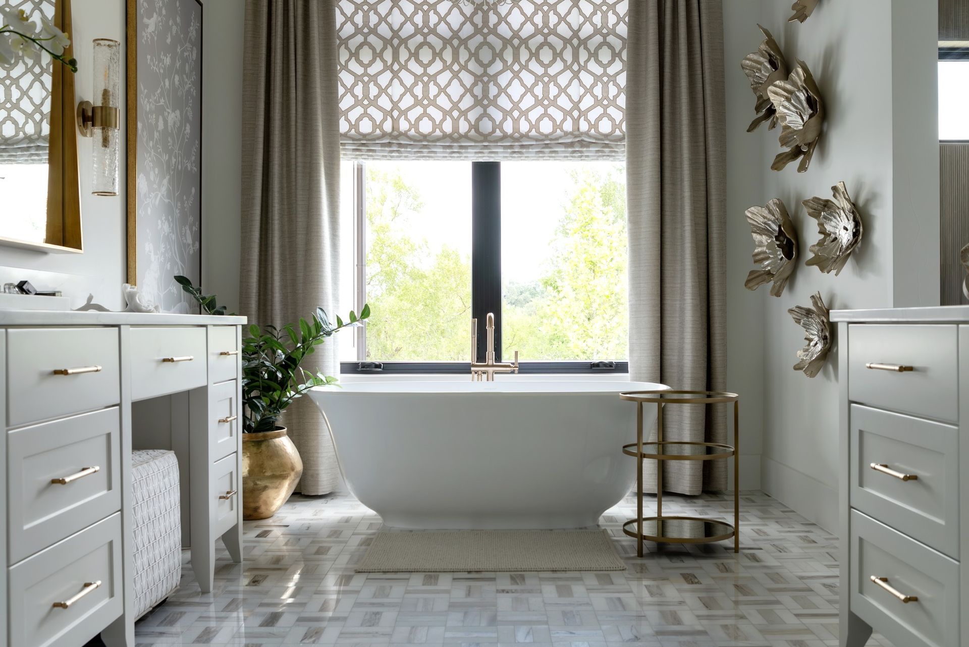 Bright bathroom with twin vanities, large window, freestanding tub, and gold accents
