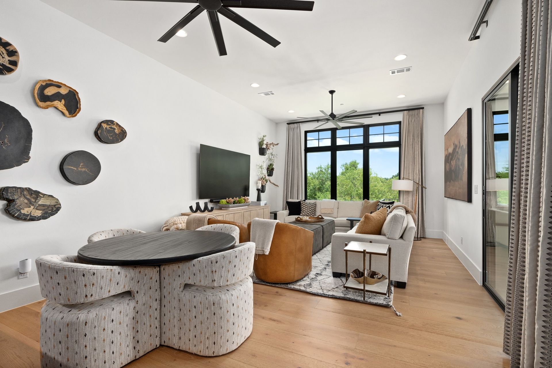 Bright modern living room with sofa, round table, TV, and large windows overlooking greenery