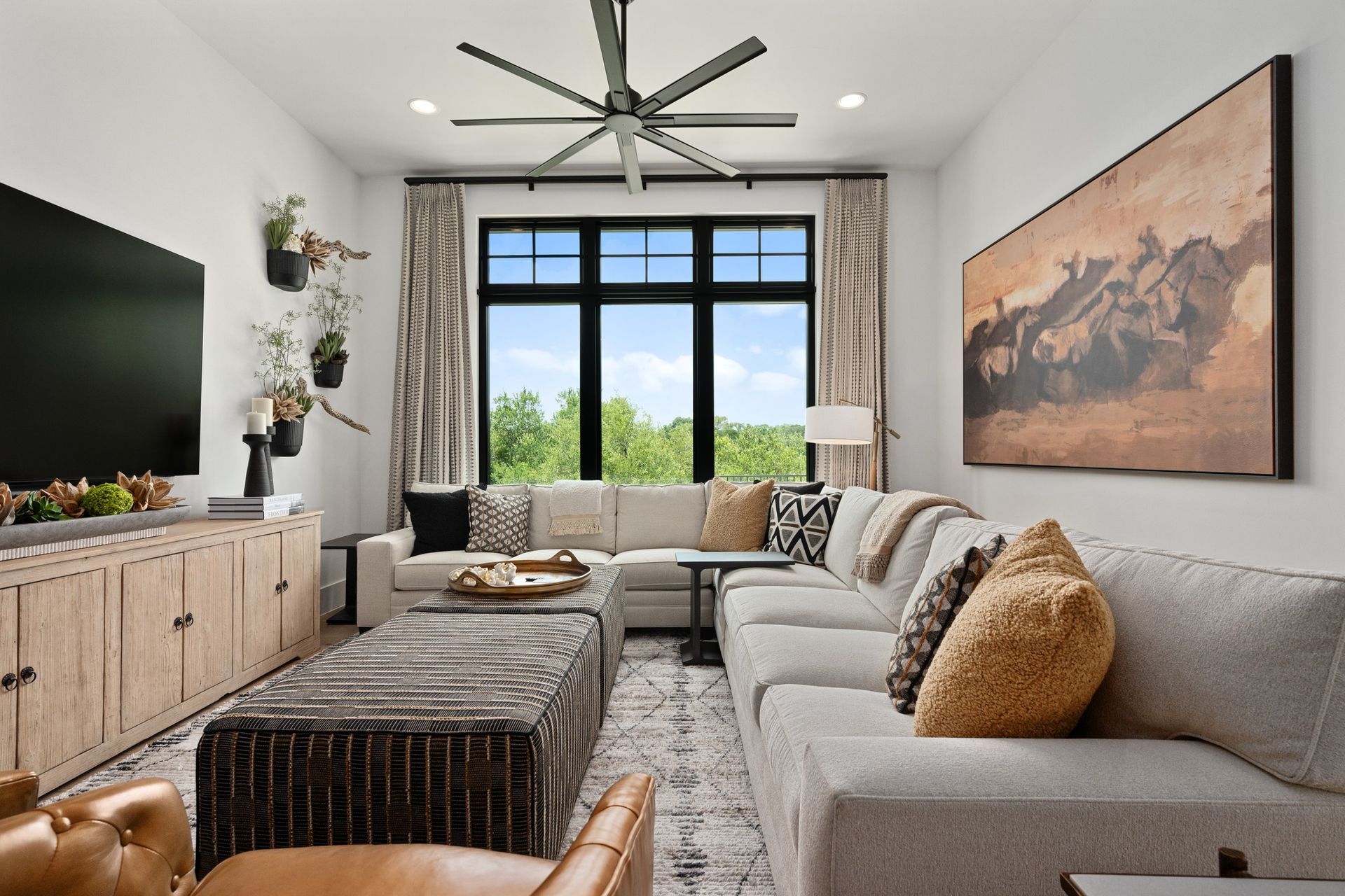 Modern living room with gray sectional sofa, woven coffee table, large window, and mountain landscape wall art.