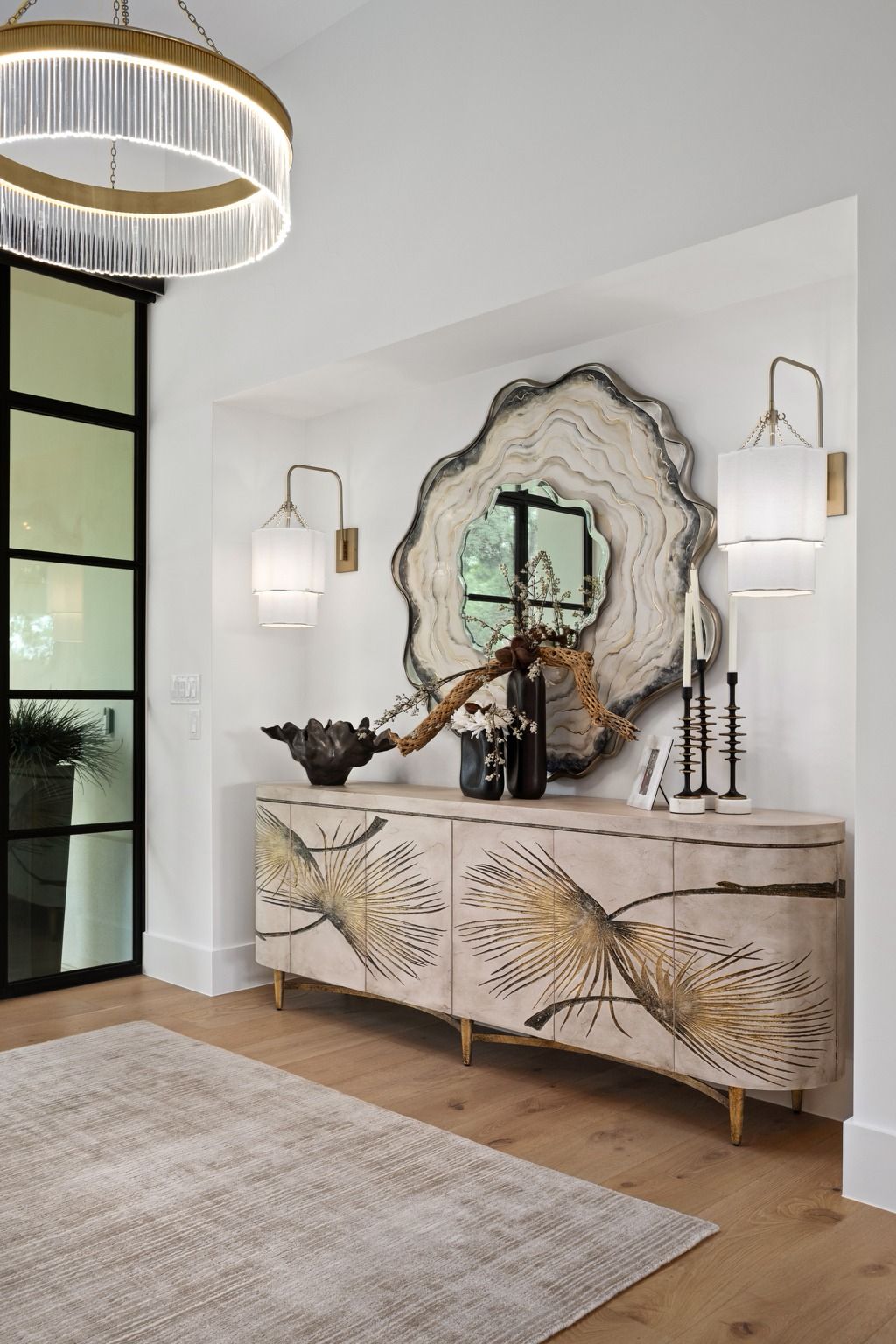 Modern entryway with patterned console, large round mirror, wall sconces, and black-framed windows