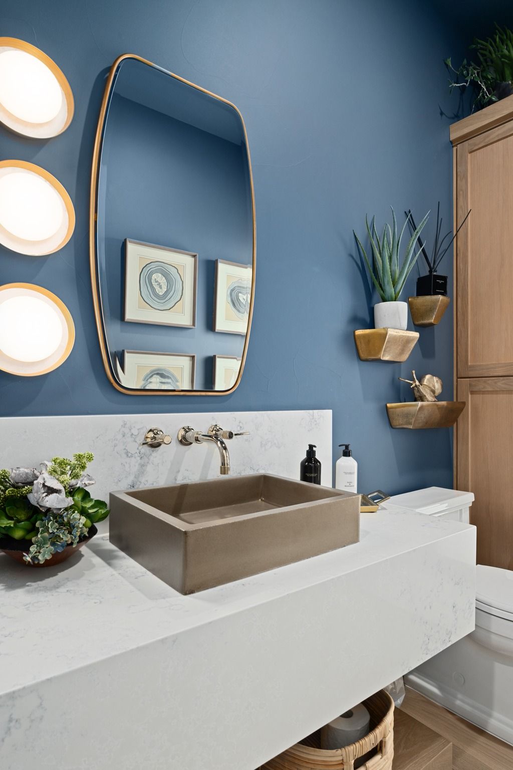 Modern bathroom vanity with blue walls, round lights, mirror, vessel sink, and wall shelves with plants
