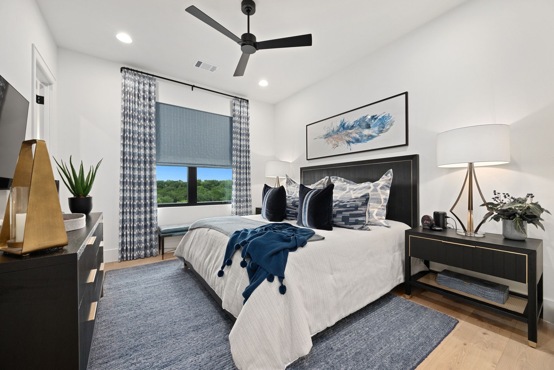 Modern bedroom with black-and-white decor, bed, ceiling fan, window, and blue accent blanket