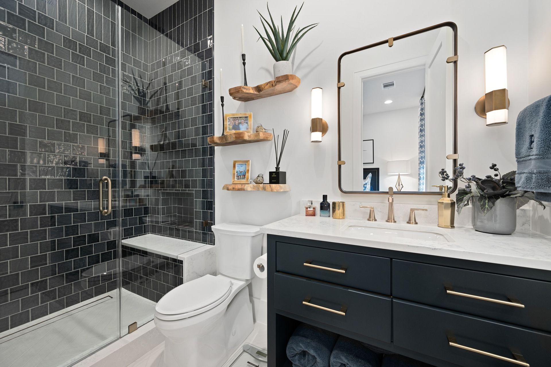 Modern bathroom with black tile shower, white tub and toilet, and dark vanity with gold fixtures