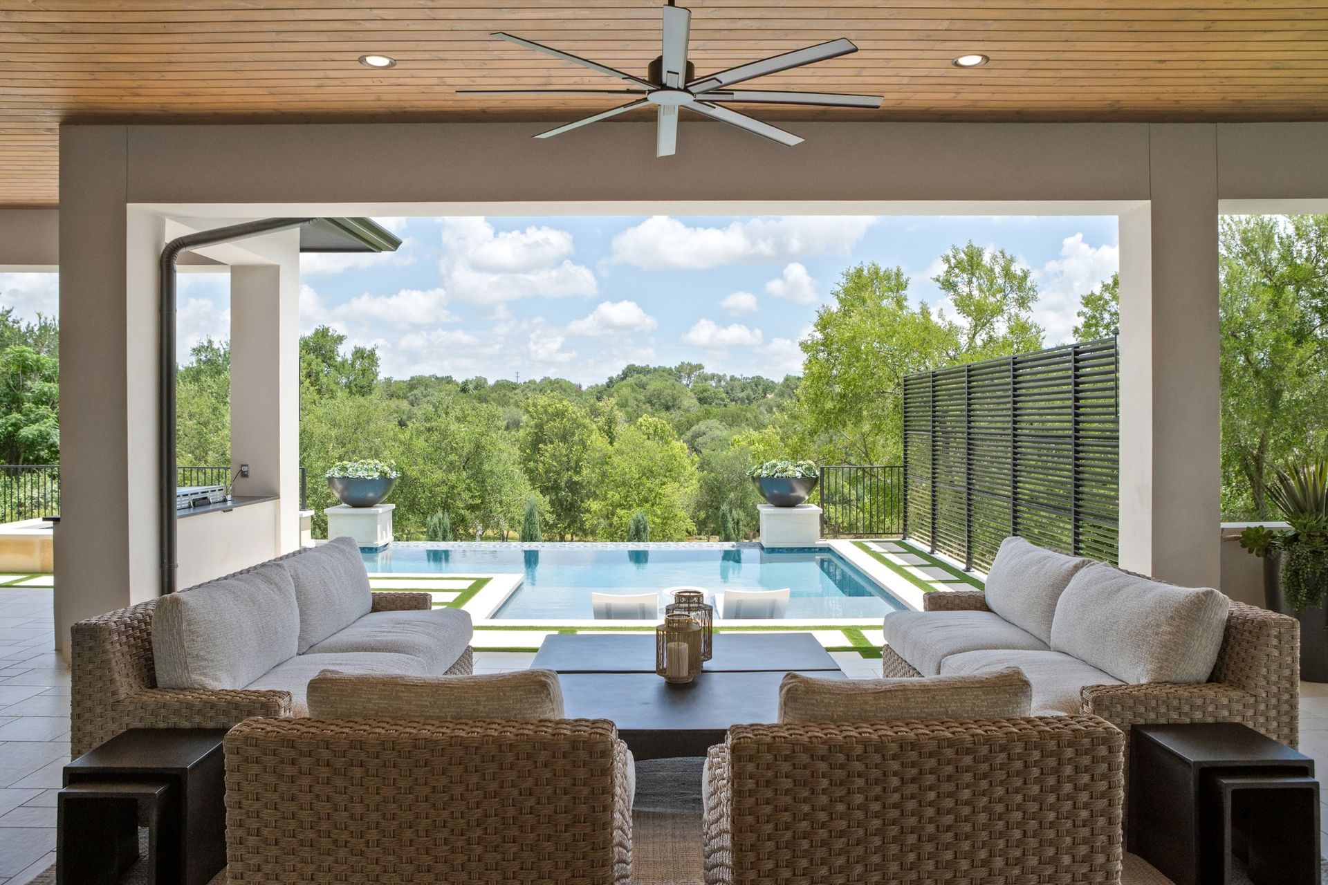Covered patio seating overlooking a pool and green landscape through wide open doors