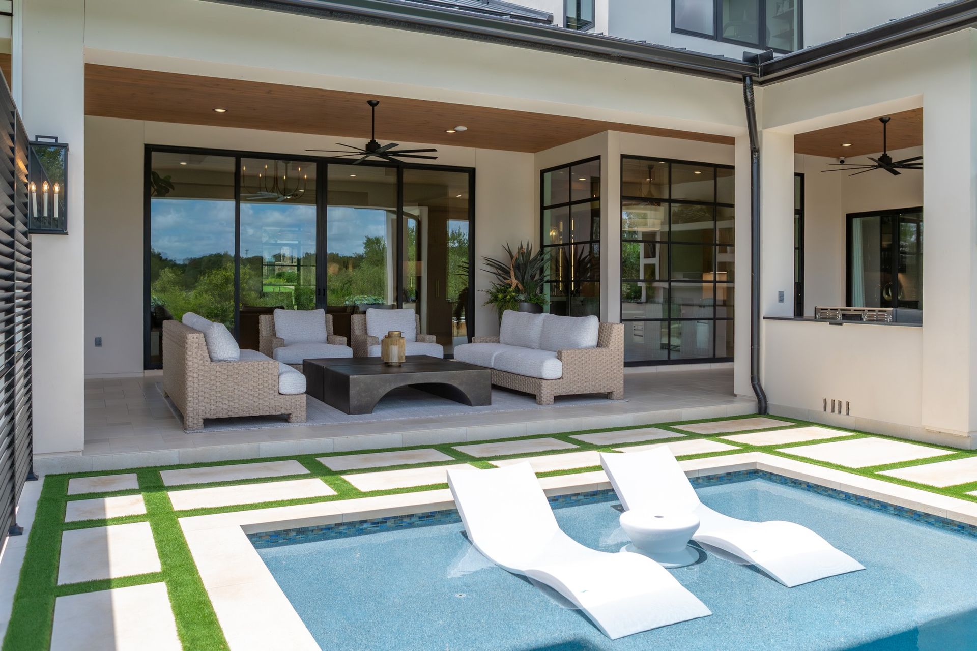 Modern patio with outdoor seating beside a small pool and sun loungers under a covered patio.
