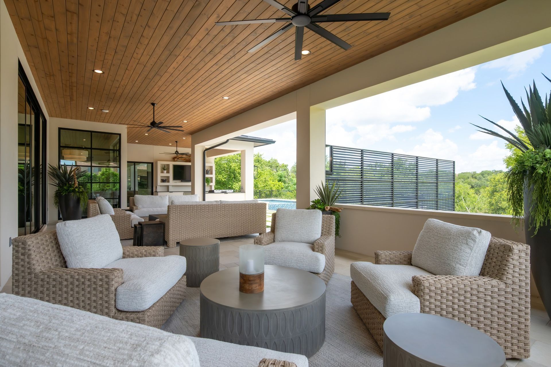 Covered patio with woven lounge chairs, round table, and ceiling fan overlooking a green yard and fence.