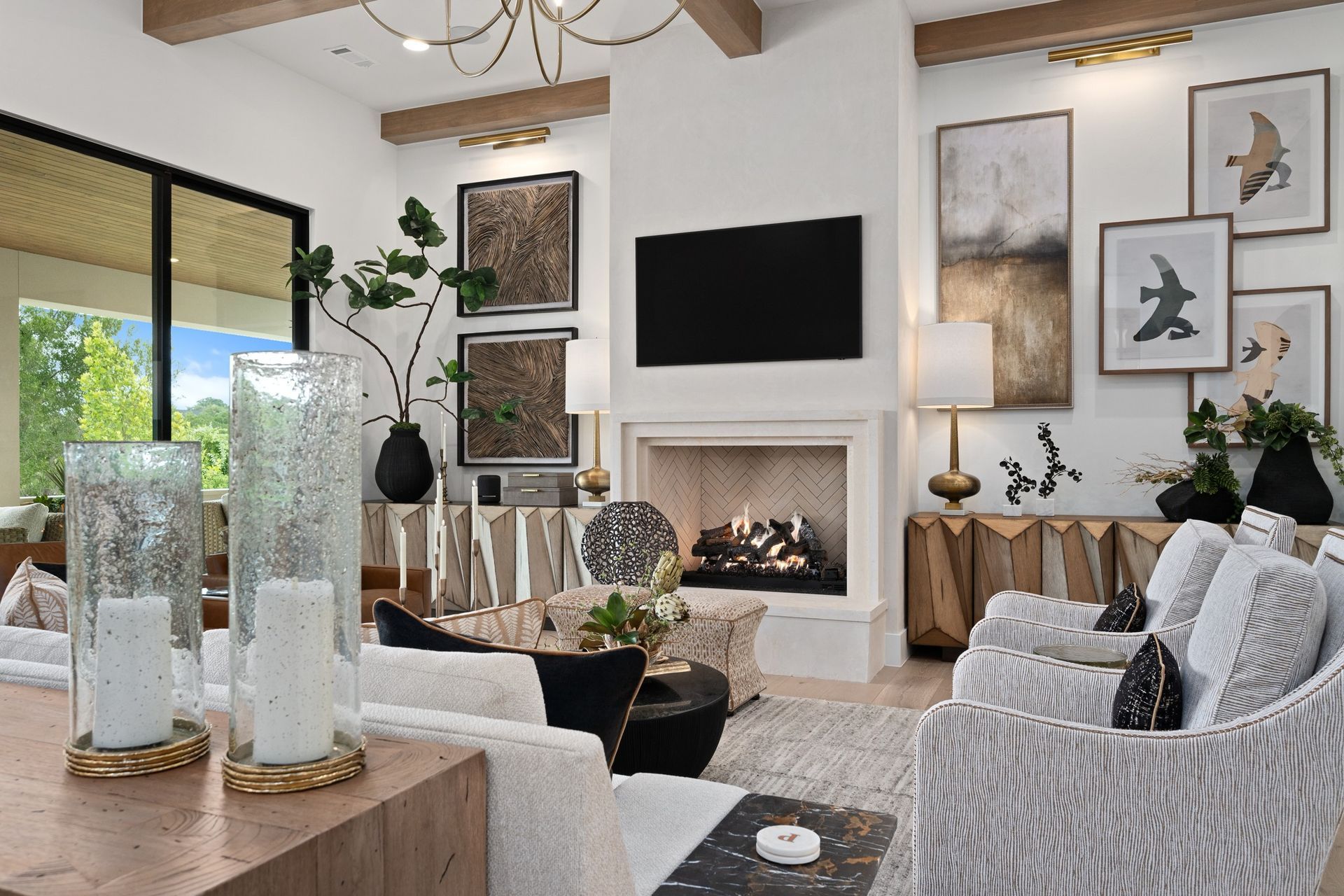 Bright modern living room with fireplace, wall-mounted TV, neutral sofas, and large windows overlooking greenery