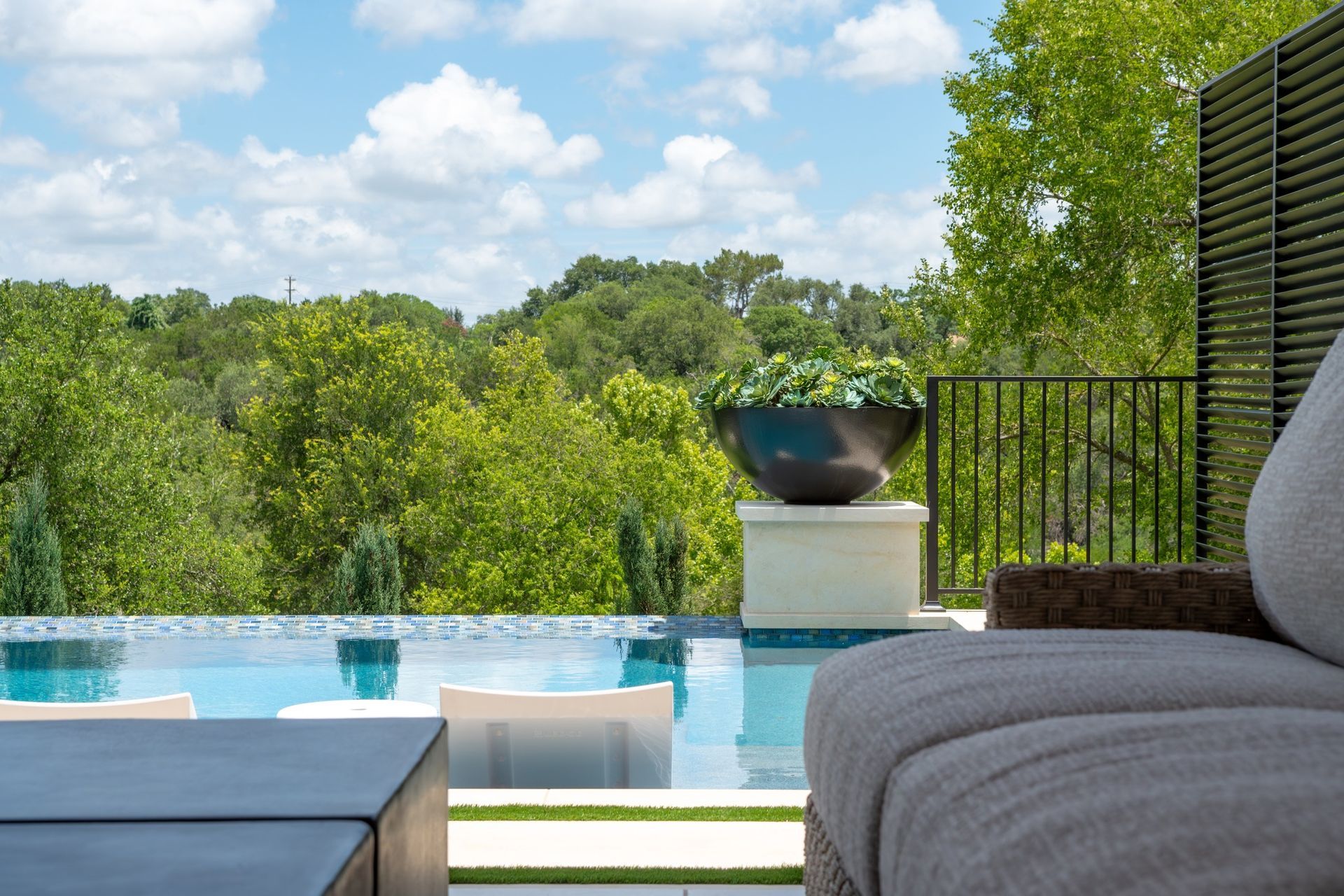 Luxury patio with pool, lounge chairs, and lush green trees under a bright blue sky