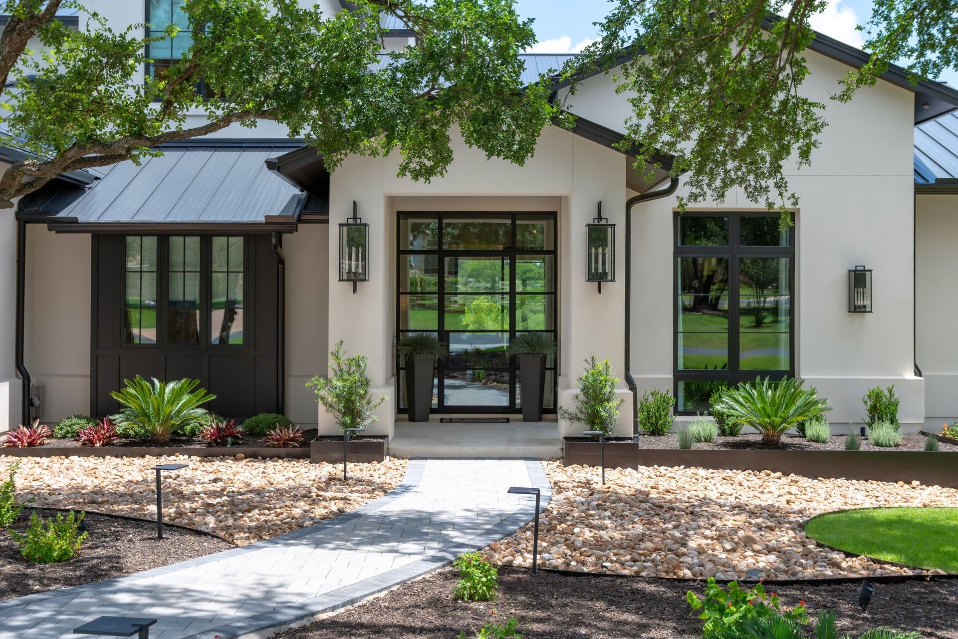 Front view of a white house with black trim, a central glass door, and a landscaped walkway