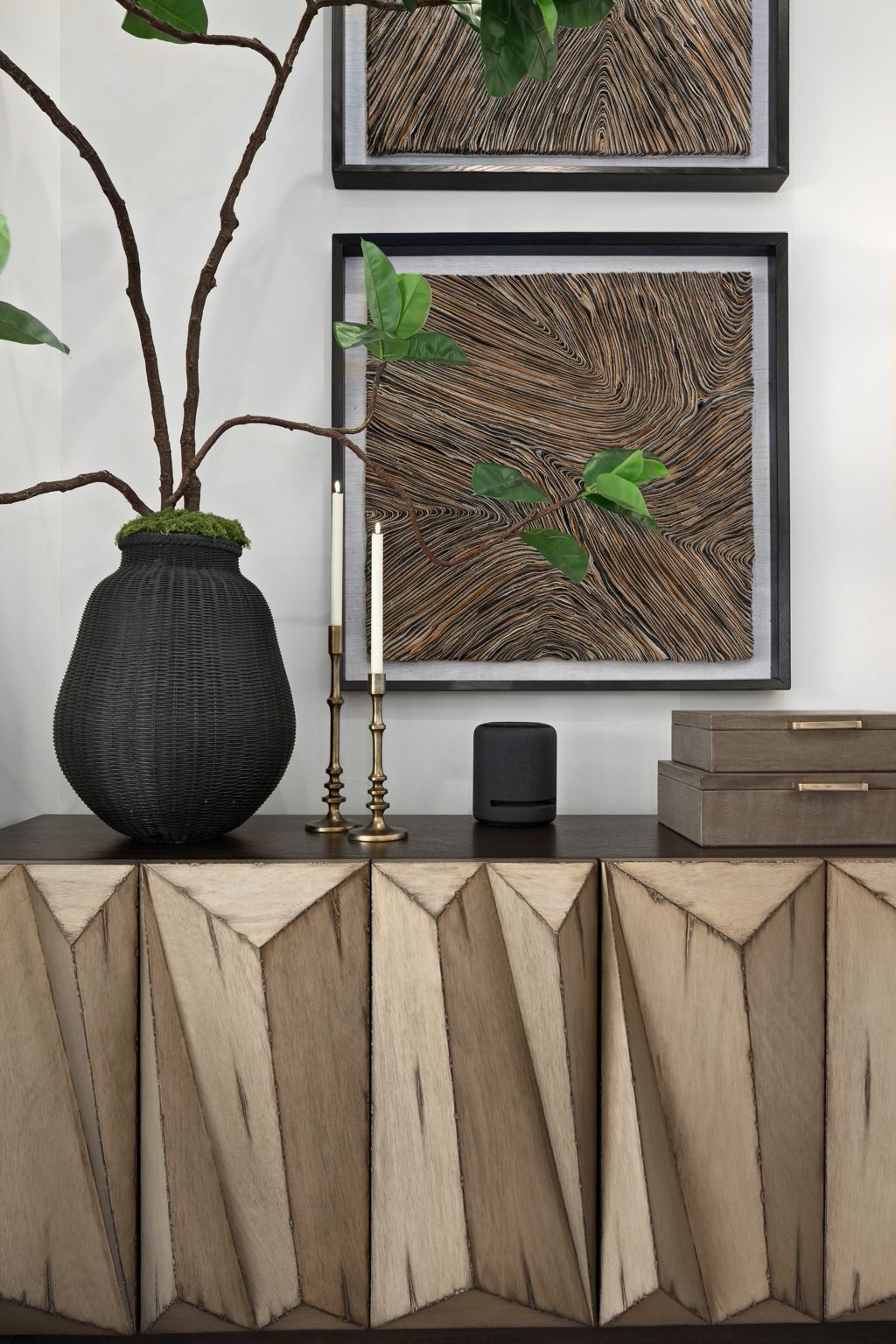 Modern console with geometric wood front, black vase, candles, and framed moss art on a white wall.