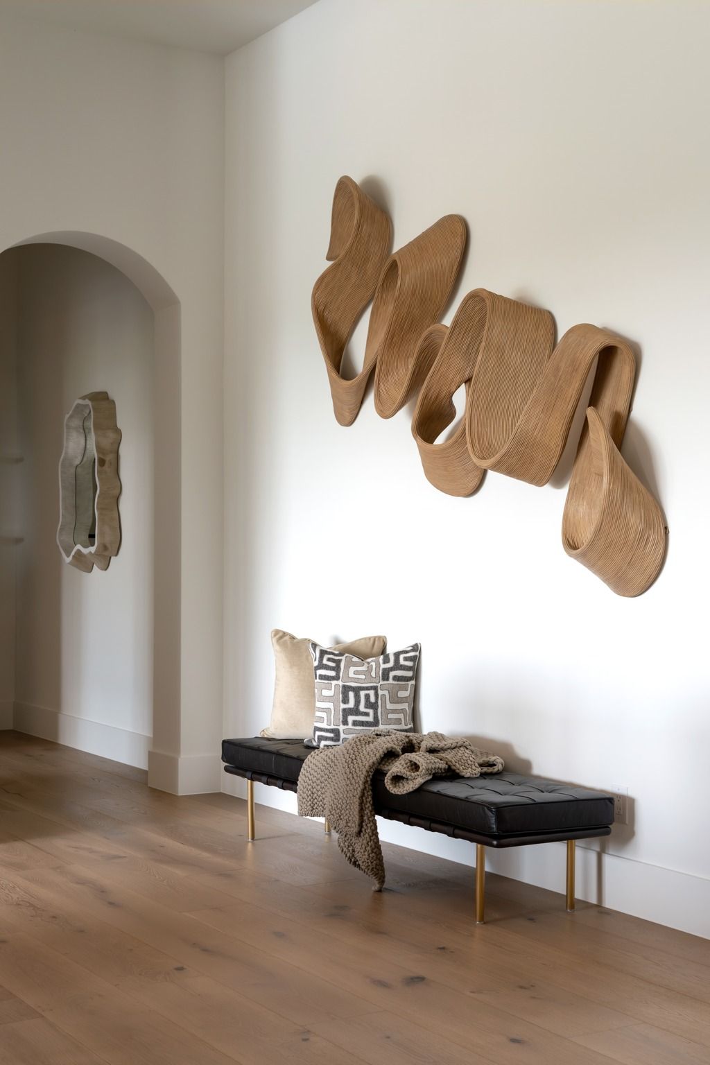 Modern hallway with abstract wall art above a black bench, pillow, throw, and arched doorway.