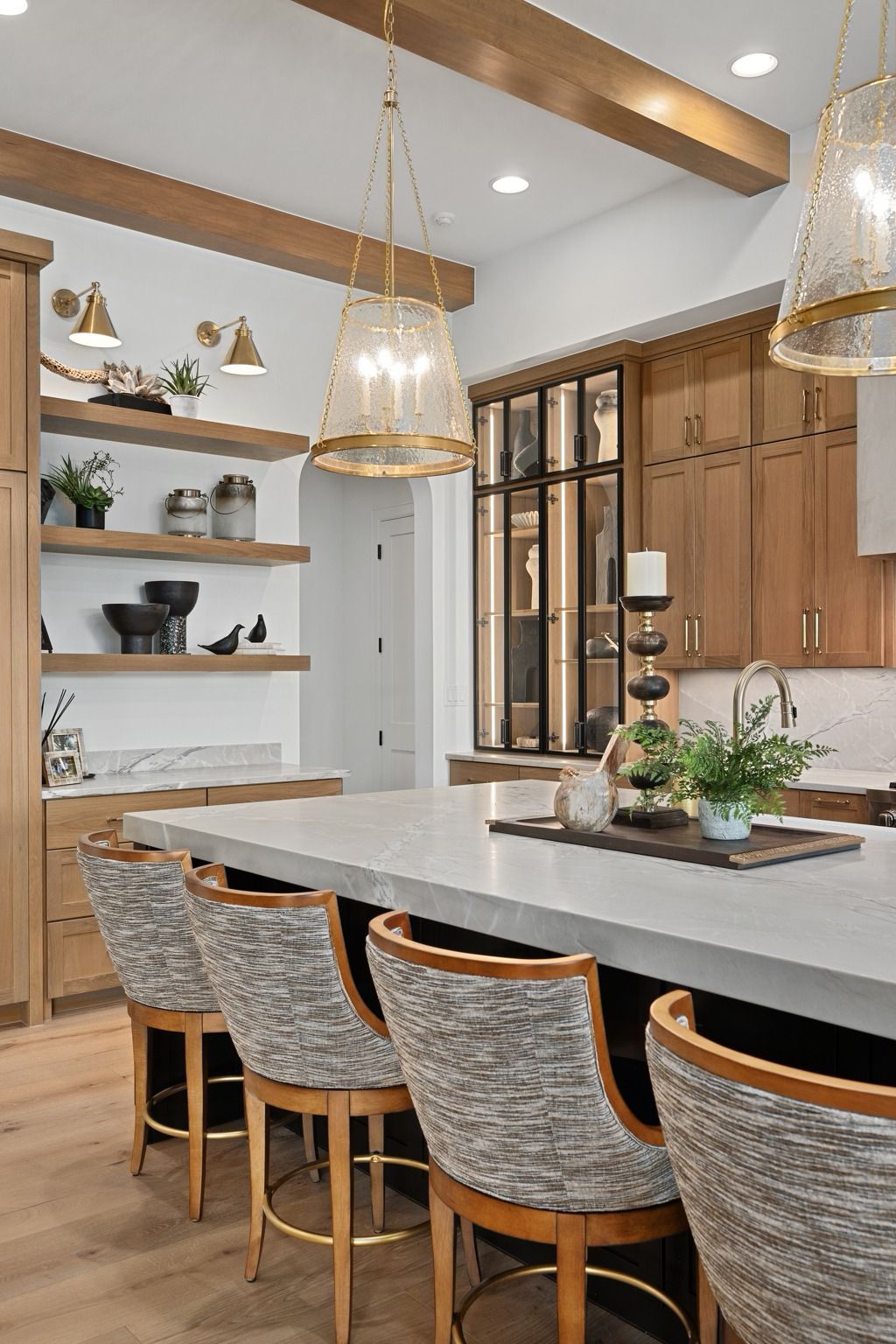 Modern kitchen with wood cabinets, marble island, woven barstools, and brass pendant lights