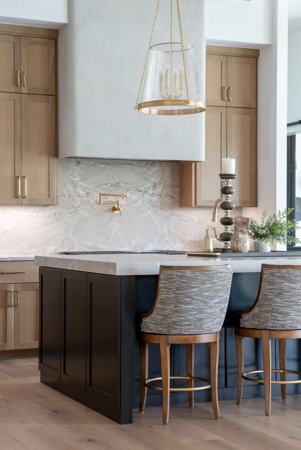 Modern kitchen with beige cabinets, dark island, gray stools, and brass pendant light