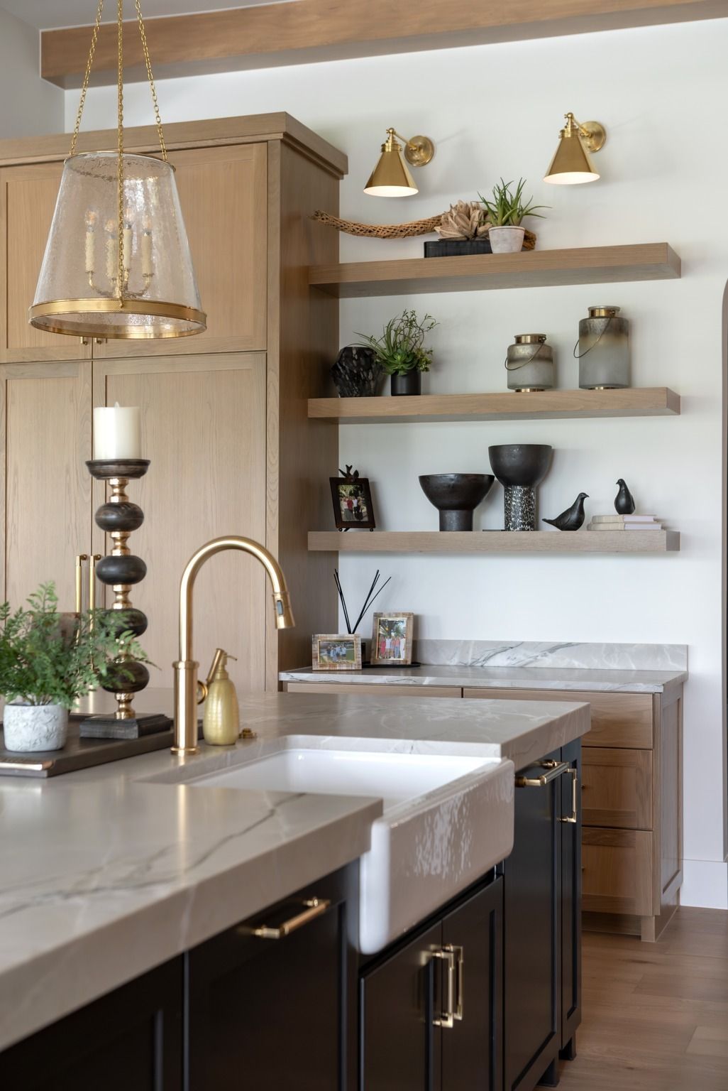 Modern kitchen with white countertops, dark cabinets, brass fixtures, and open shelves with decor
