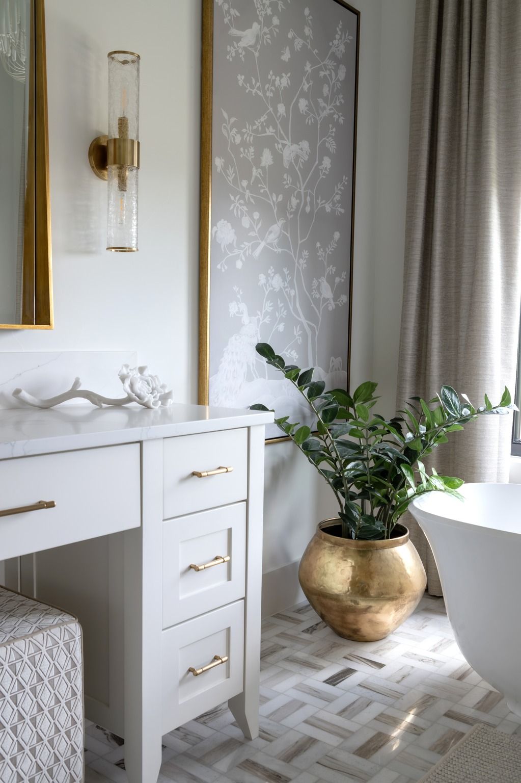 Bright bathroom vanity with gold plant pot, white tub, patterned floor, and a large window.