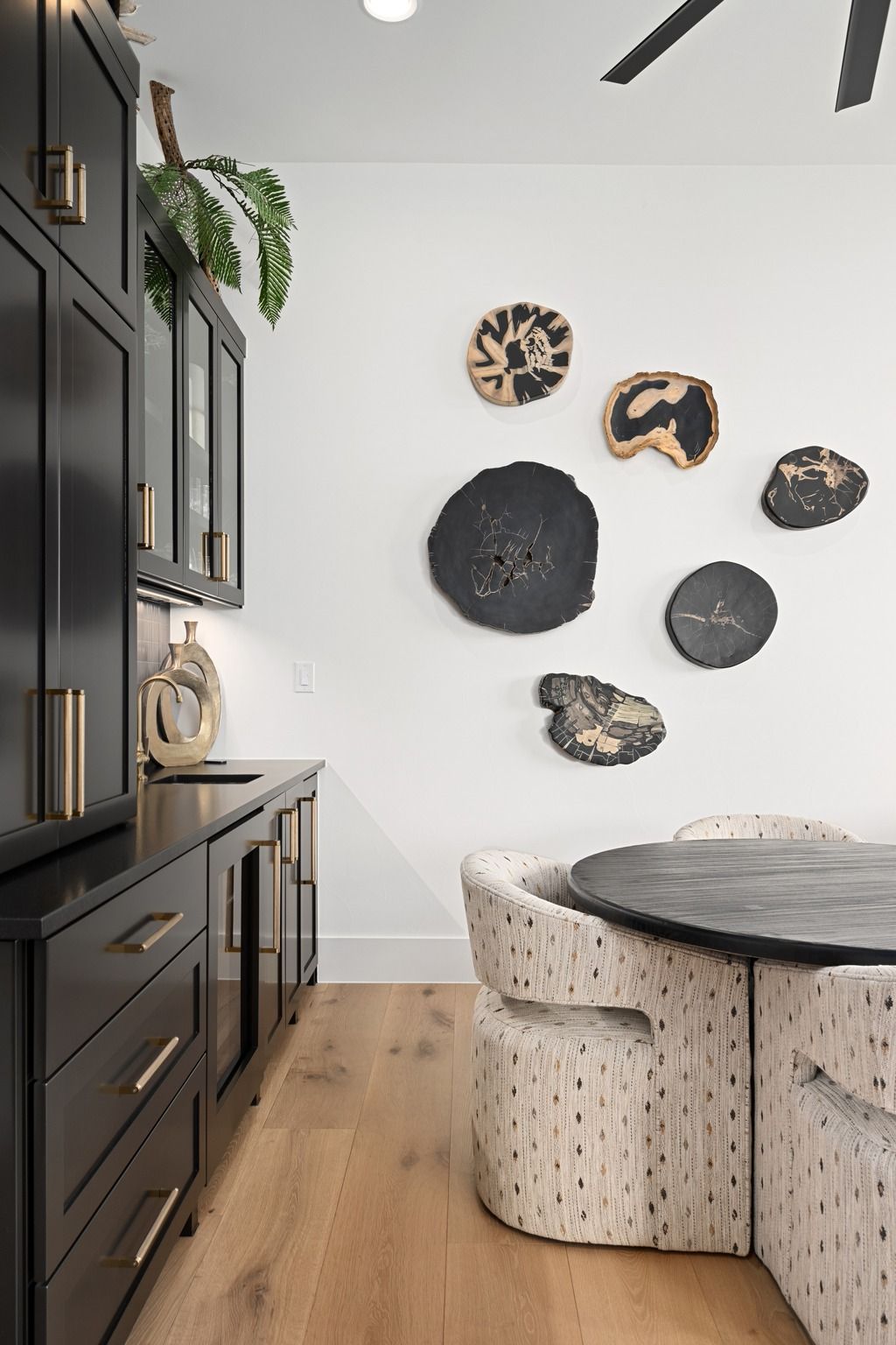 Modern dining nook with black cabinets, round table, beige chairs, and wall art on a white wall