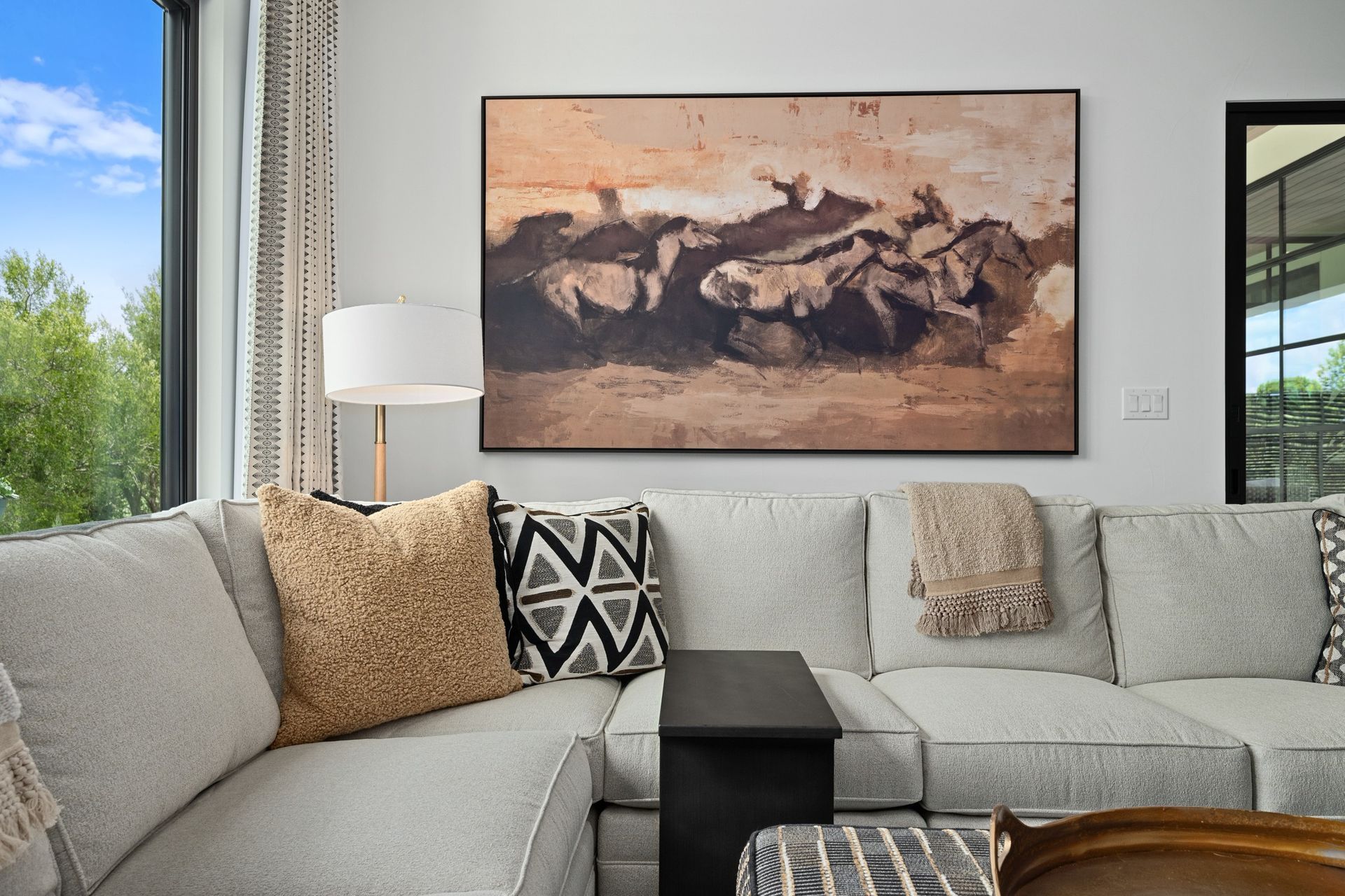 Modern living room with gray sectional sofa, patterned pillows, floor lamp, and large abstract painting