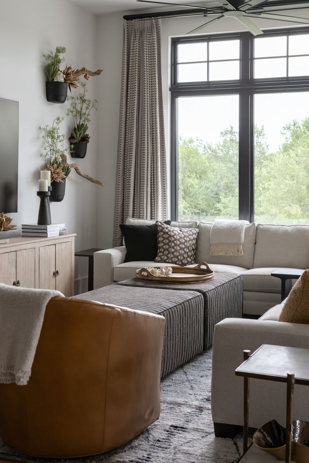 Bright living room with large window, gray sofa, tan chair, and hanging plants