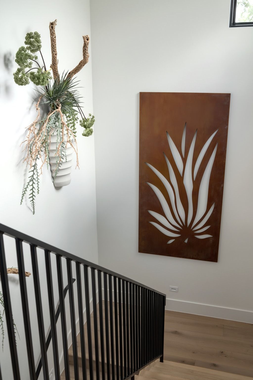 Stairwell with black railing, hanging plant, and a rust-colored wall art panel with white leaf design.
