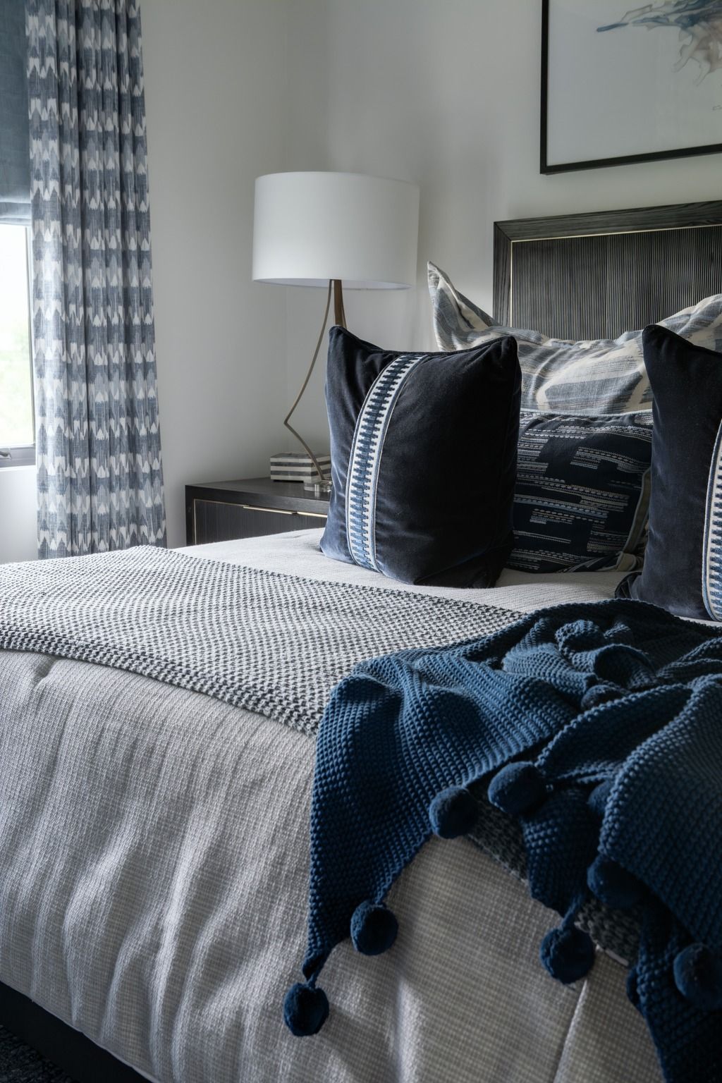 Cozy bedroom with a neatly made bed, navy throw blanket, and white lamp by a window
