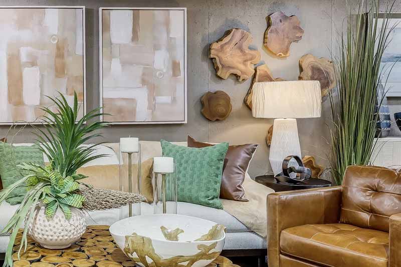 Stylish living room with tan leather chairs, cream sofa, green pillows, plants, and abstract wall art.