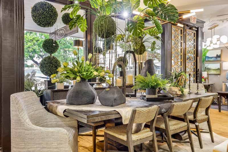 Elegant dining room with a wooden table, woven chairs, and hanging greenery under warm lighting
