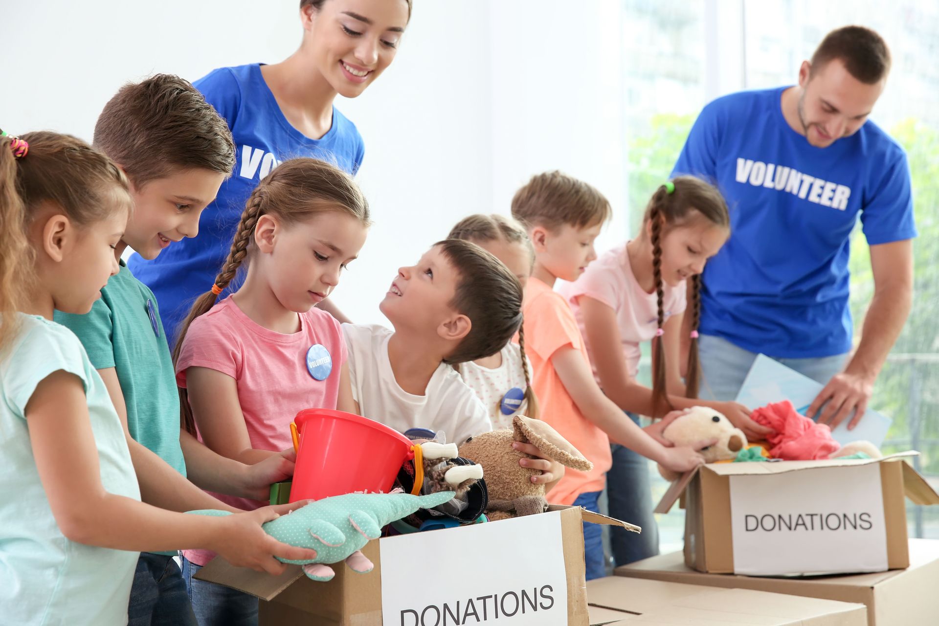 Children and volunteers sorting donations into boxes; bright interior.