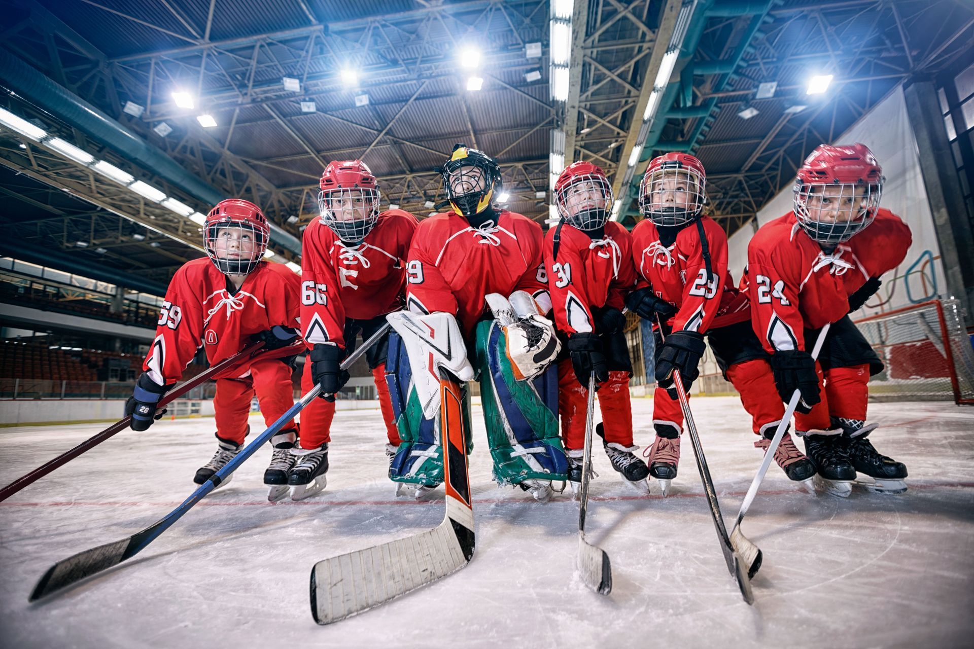 Youth hockey team in red uniforms on ice, holding sticks.