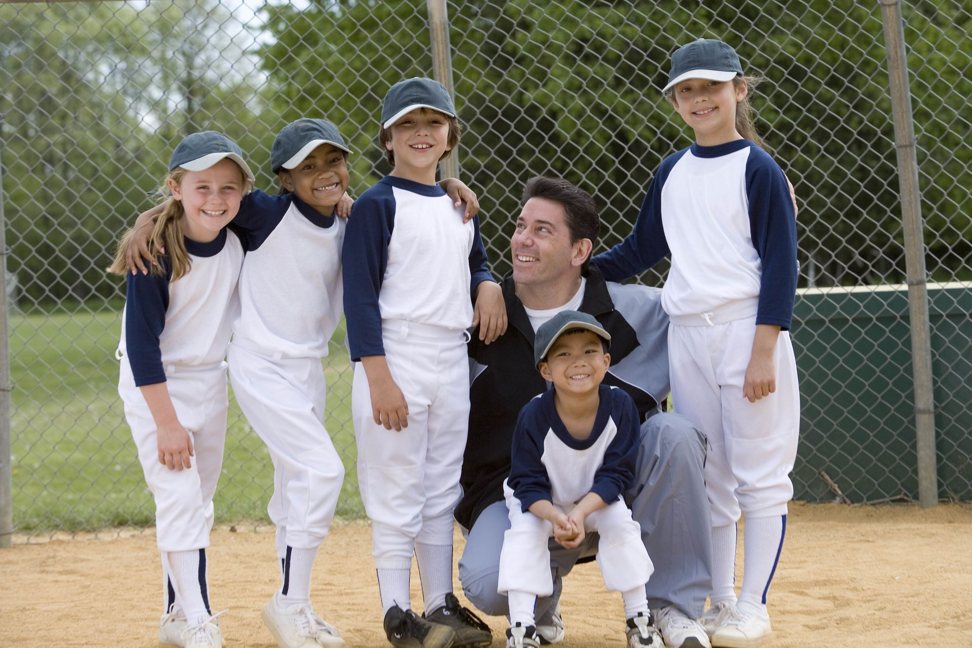 Baseball team of children and coach posing on a baseball field, wearing uniforms.
