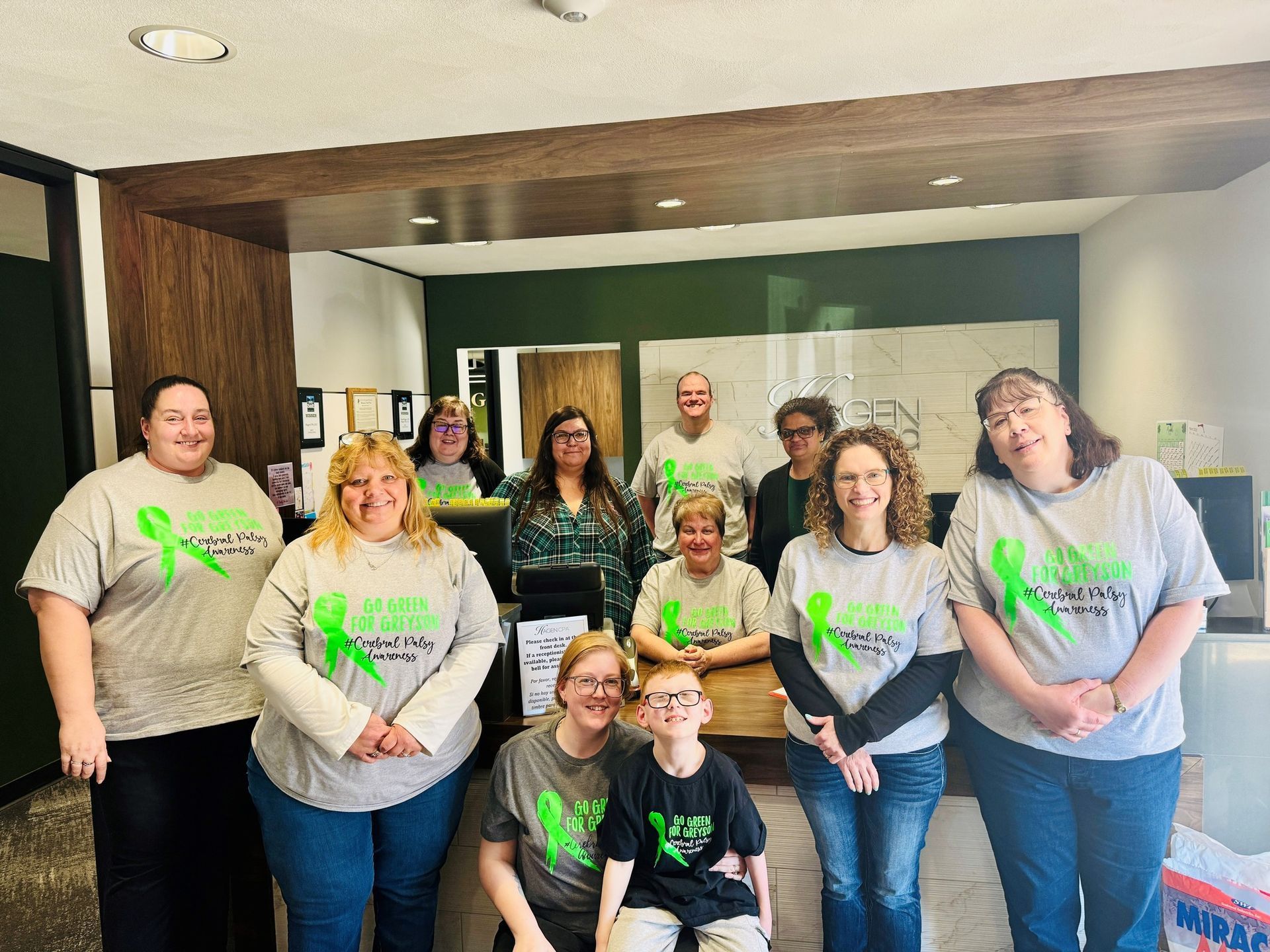 Group wearing green ribbon shirts pose in office setting.