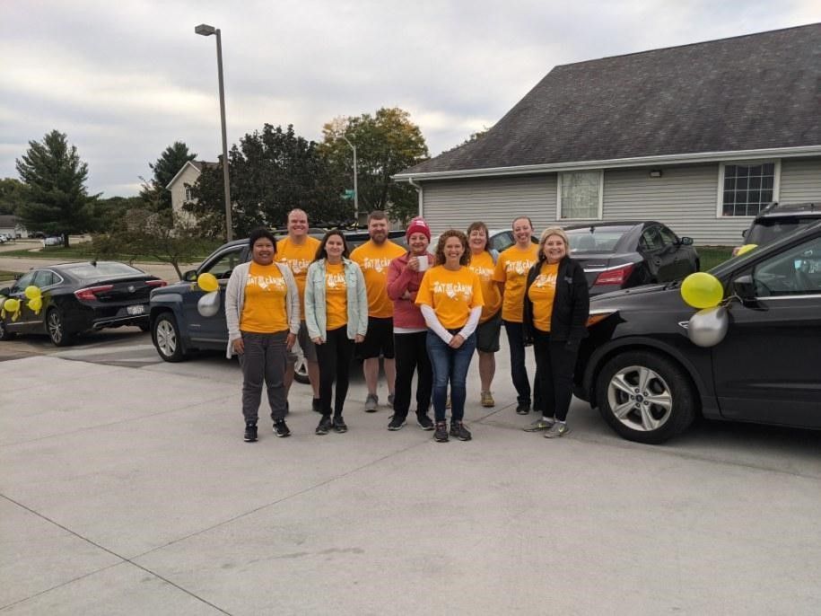 Group of people wearing yellow shirts stand outside next to cars decorated with balloons.