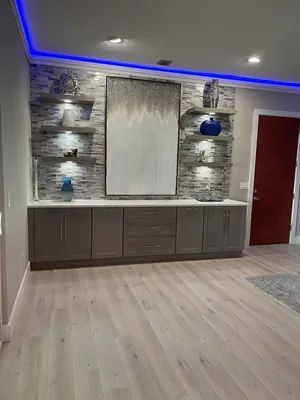 Modern living room with stone accent wall, blue LED ceiling lights, gray cabinets, and a red door