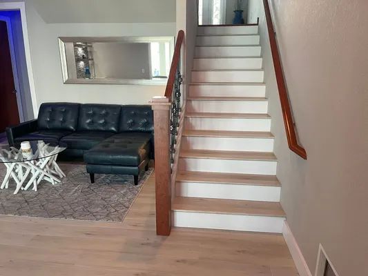 Living room with black sofa, white coffee tables, and a staircase with wooden handrail
