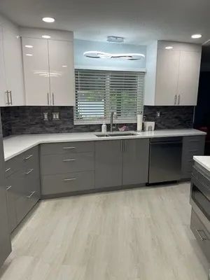 Modern kitchen with gray cabinets, white counters, black backsplash, and a window over the sink.