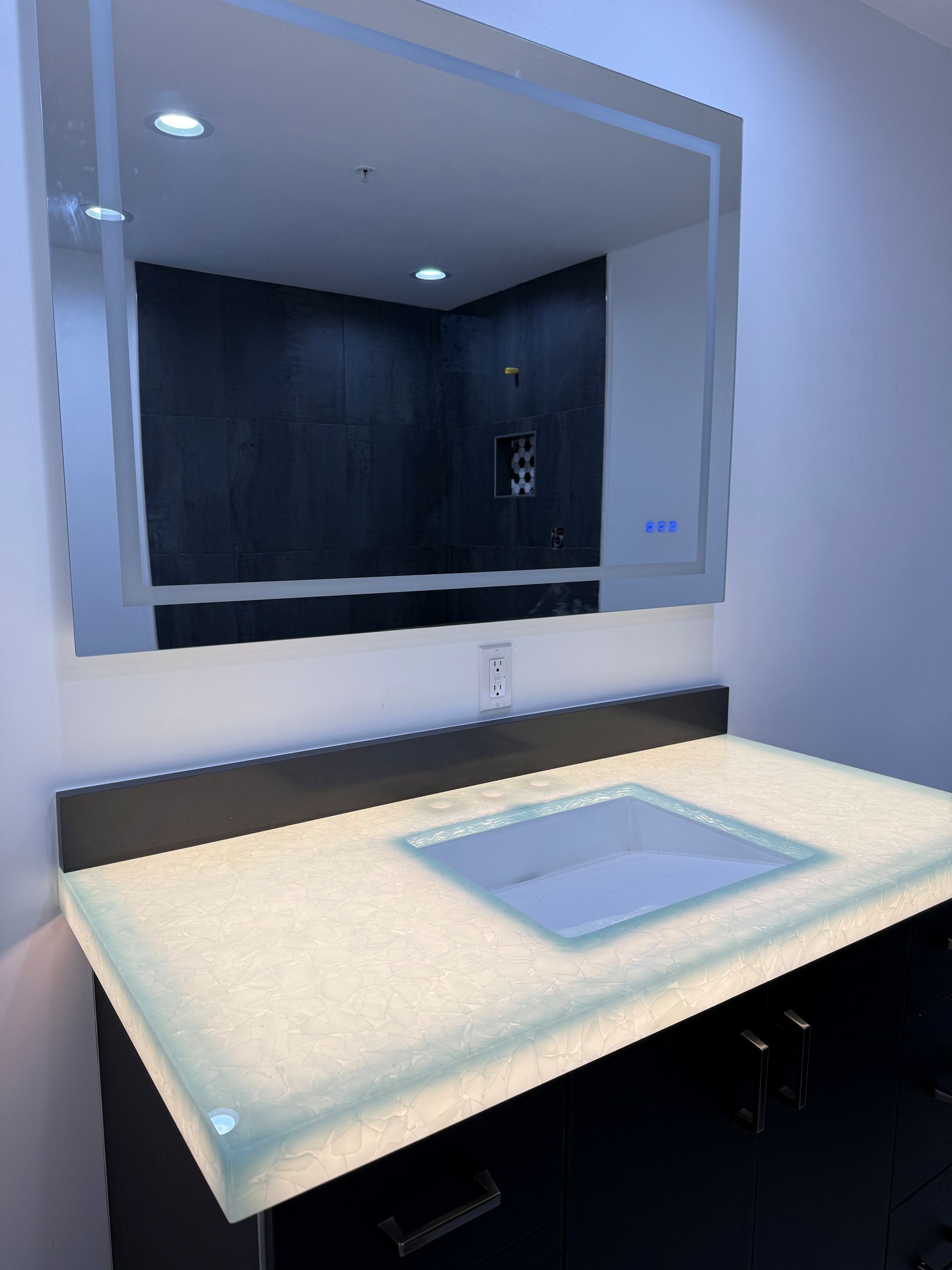 Modern bathroom vanity with illuminated mirror, countertop, and built-in sink under dark cabinet