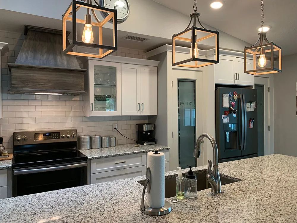 Modern kitchen with white cabinets, black appliances, pendant lights, and a speckled island counter