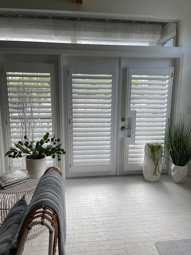 Bright white sunroom with louvered doors, potted plants, and a chair in the foreground