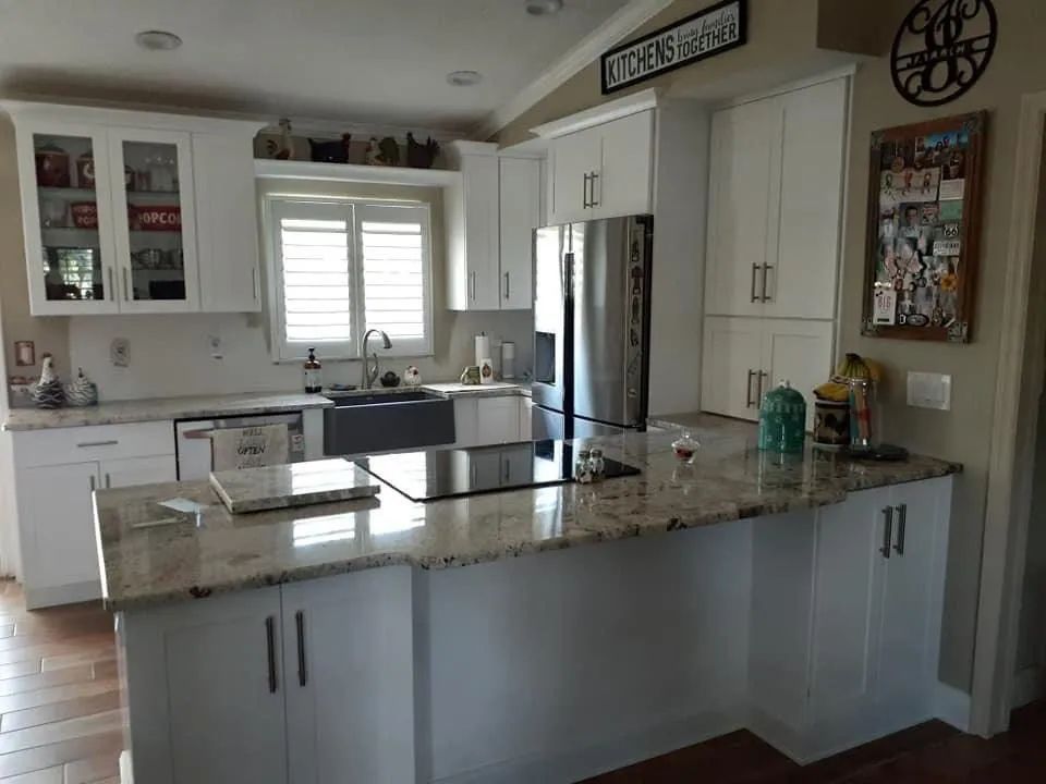 Modern kitchen with white cabinets, granite island, stainless-steel fridge, and window above the sink